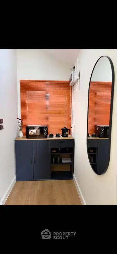 Modern kitchen corner with sleek cabinetry and vibrant orange blinds, featuring a microwave and coffee maker.