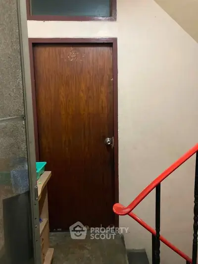 Simple interior hallway with wooden door and red handrail, ideal for budget-friendly housing.