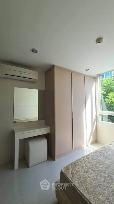 Bright bedroom with large window, built-in wardrobe, and air conditioning unit.