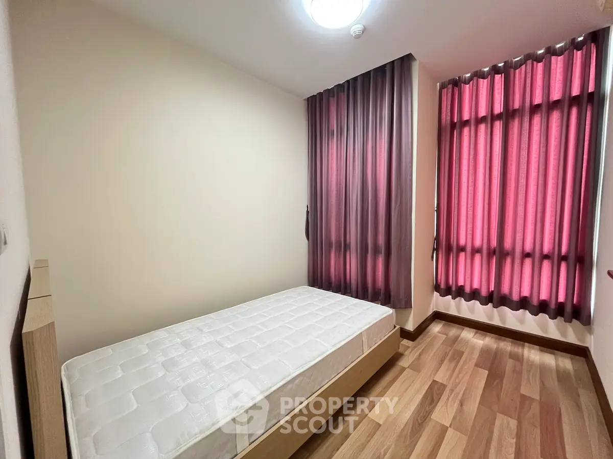 Cozy bedroom with wooden flooring and natural light from large windows, perfect for relaxation.