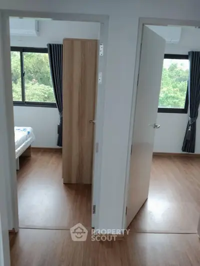Modern apartment with two bedrooms featuring large windows and wooden flooring, offering a serene green view.