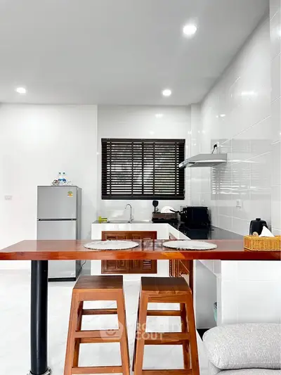 Modern kitchen with sleek design, featuring a breakfast bar, stools, and stainless steel appliances.