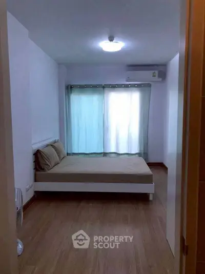 Cozy bedroom with wooden flooring and natural light from large window.