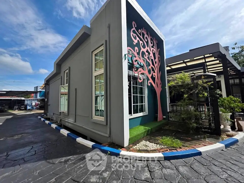 Modern building exterior with unique tree mural and paved driveway under blue sky.