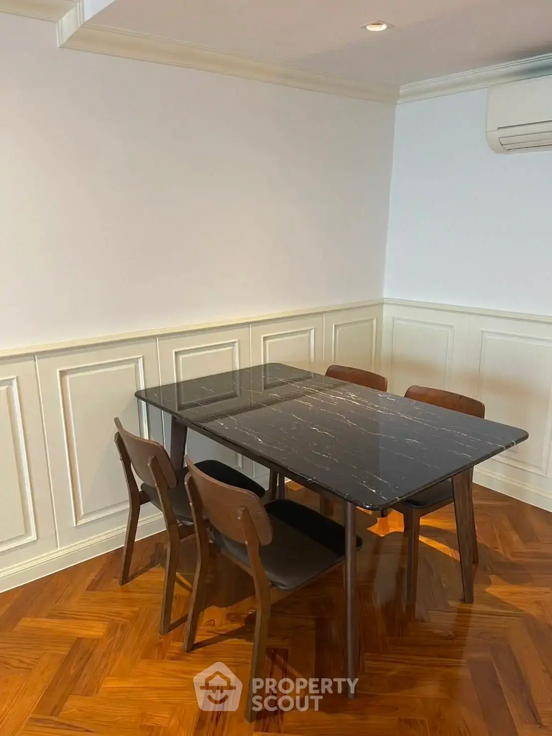 Elegant dining area with modern black marble table and wooden chairs on polished parquet flooring.