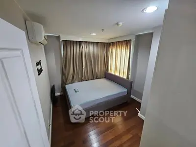 Cozy bedroom with wooden flooring and natural light, featuring a comfortable bed and air conditioning.