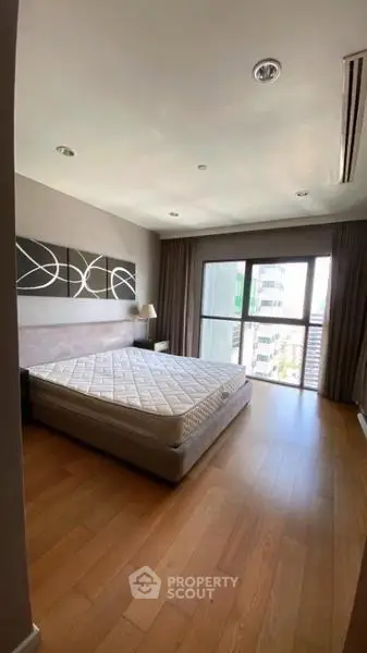 Spacious bedroom with large window and modern decor in high-rise apartment.