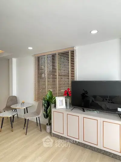 Modern living room with stylish decor and flat-screen TV, featuring elegant furniture and wooden blinds.