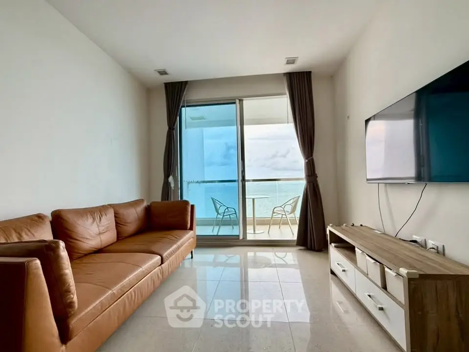 Modern living room with ocean view, leather sofa, and wall-mounted TV, leading to a balcony.