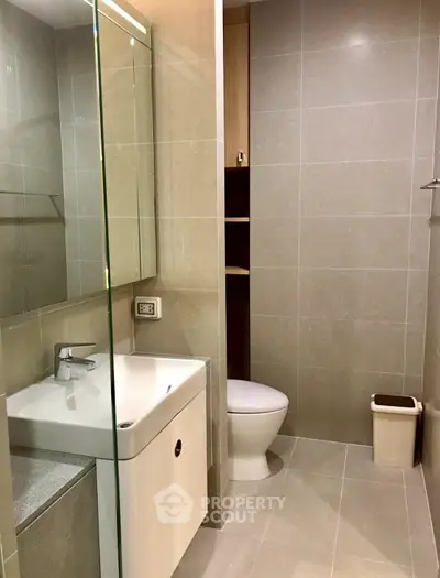 Modern bathroom with sleek design and neutral tiles, featuring a compact sink and toilet.
