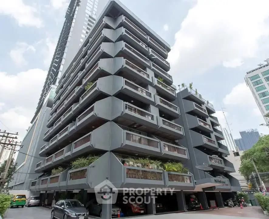 Modern multi-story residential building with balconies and parking area in urban setting.