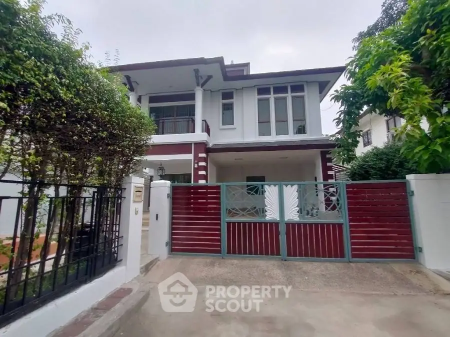 Charming two-story house with gated entrance and lush greenery in a serene neighborhood.