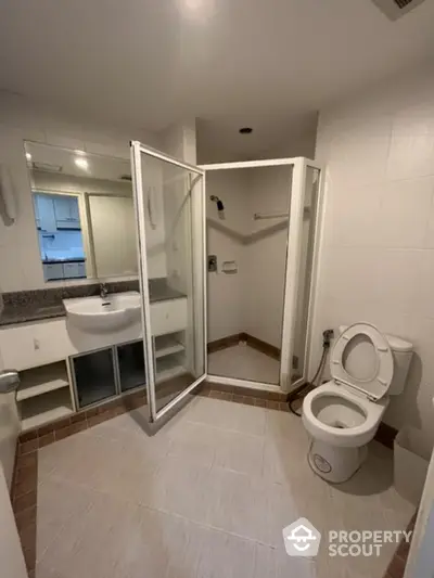 Spacious bathroom with white tiles, large mirror, and glass shower enclosure, offering a clean and bright space for relaxation.