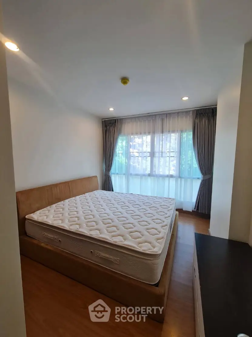 Spacious bedroom with large window and elegant curtains, featuring a comfortable bed and wooden flooring.