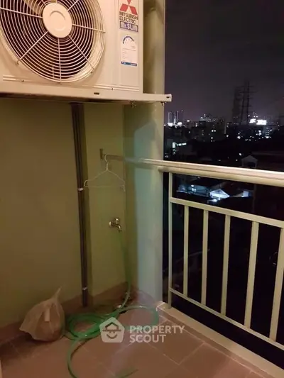 Night view from a balcony with air conditioning unit and city skyline.