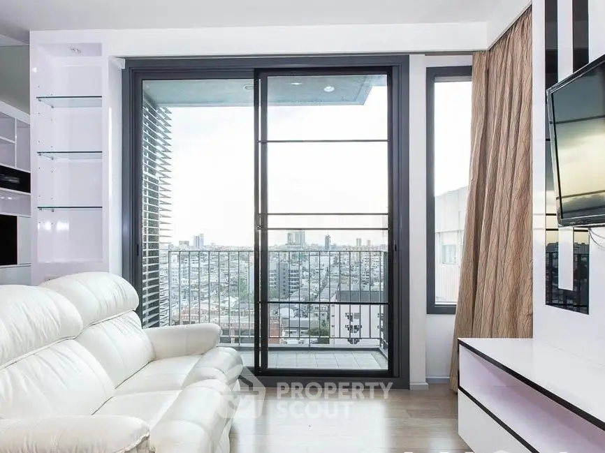 Modern living room with city view, large windows, and sleek white furniture.