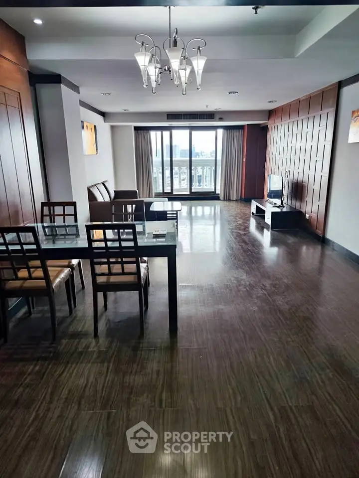 Spacious living room with elegant wooden flooring and modern furniture, featuring a large window with city views.