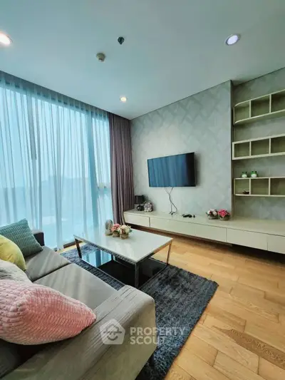 Modern living room with large windows, stylish decor, and wall-mounted TV.