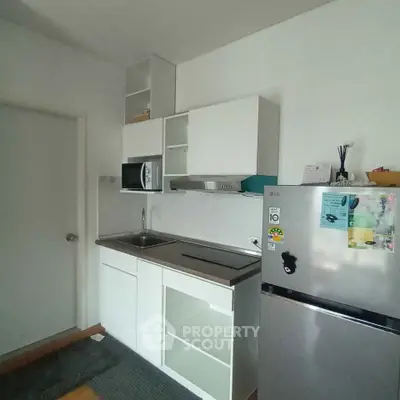 Modern compact kitchen with sleek cabinetry and stainless steel fridge in a cozy apartment.