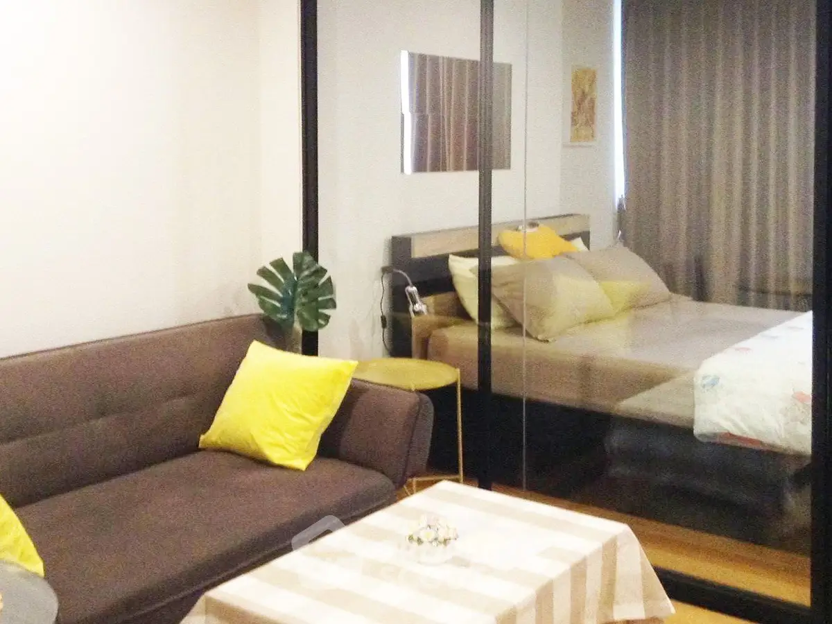 Modern studio apartment with cozy living area and stylish bedroom separated by glass partition.