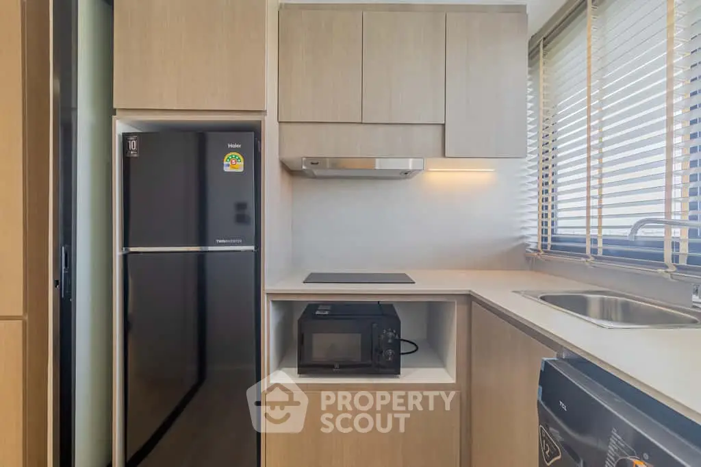 Modern kitchen with sleek appliances and wooden cabinetry, featuring a fridge, microwave, and electric stove.