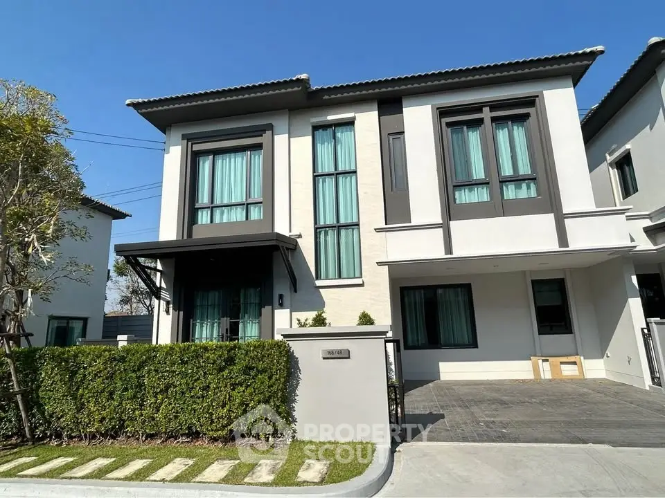 Modern two-story house with large windows and manicured lawn in a suburban neighborhood.