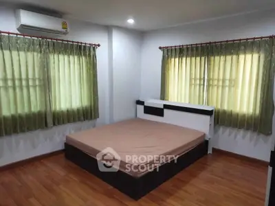 Cozy bedroom with wooden flooring and natural light from two windows, featuring a modern bed and air conditioning.