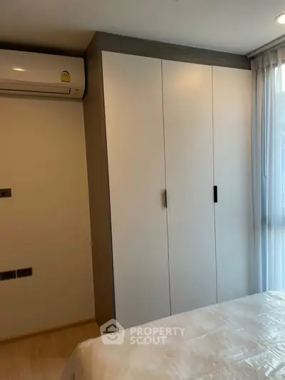 Modern bedroom with built-in wardrobe and air conditioning, featuring natural light from large window.