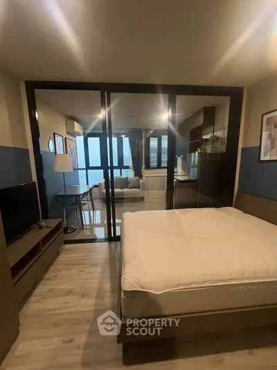 Modern bedroom with glass partition leading to a stylish living area, featuring sleek furniture and natural light.