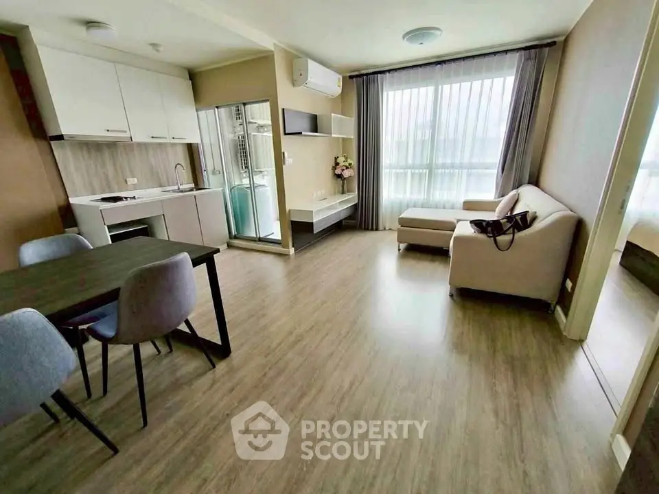 Modern open-plan living room with dining area and large window, featuring stylish furniture and wood flooring.