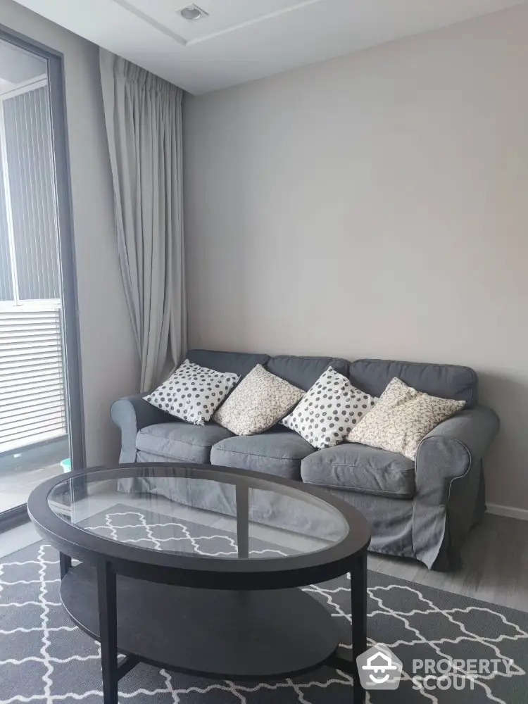 Elegant living room with plush grey sofa adorned with patterned cushions, sleek glass-top coffee table, and chic grey patterned rug, offering a serene urban retreat.