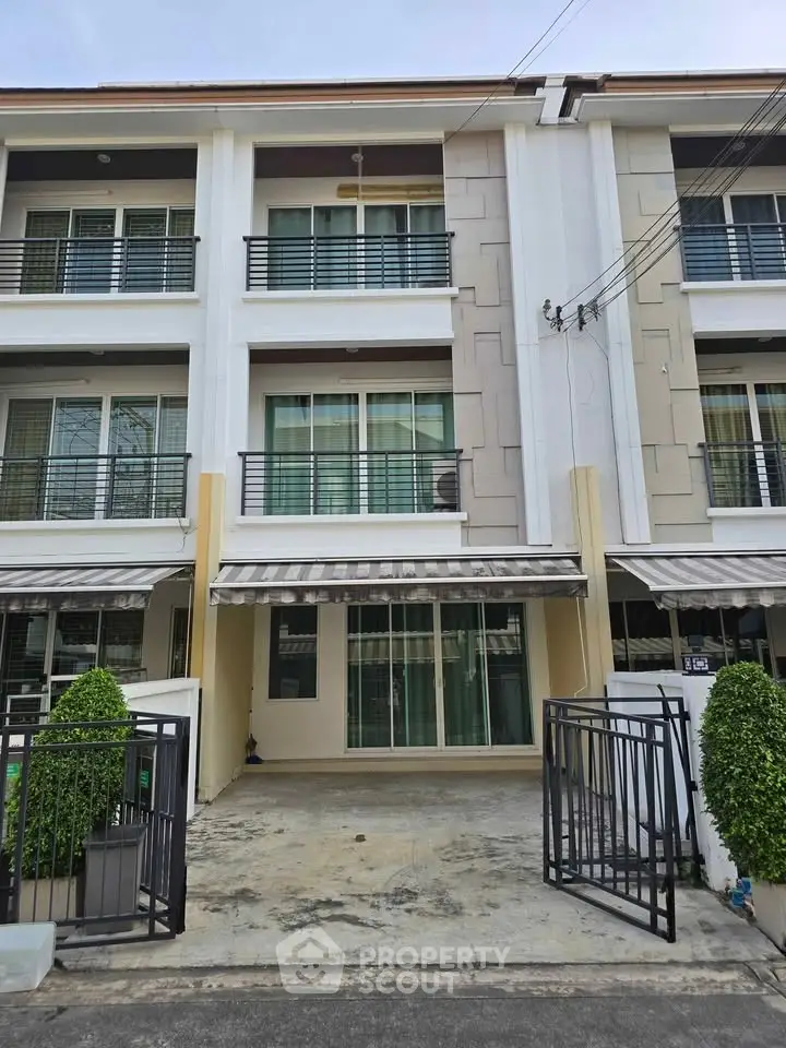 Modern three-story townhouse with gated entrance and balcony in a suburban neighborhood.