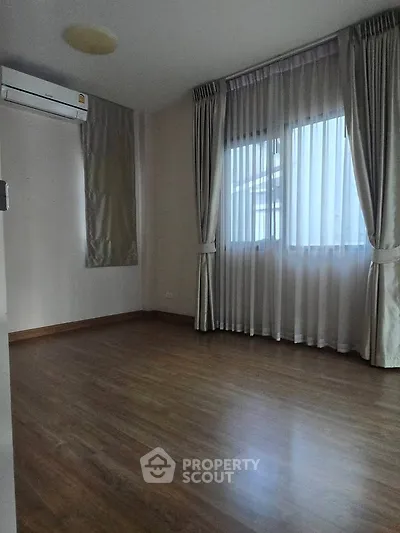 Spacious empty room with wooden flooring and large windows, perfect for customization.