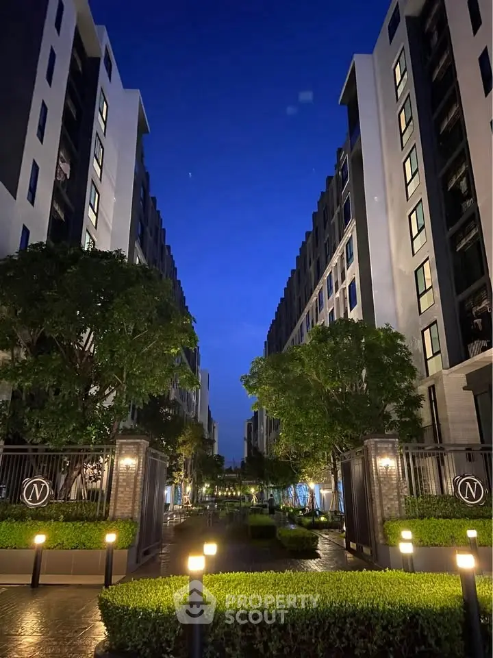 Stunning evening view of modern apartment complex with lush greenery and illuminated pathways.