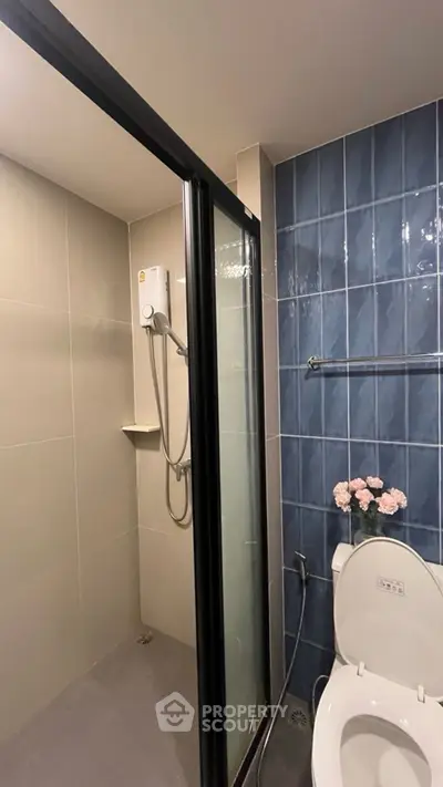 Modern bathroom with shower and toilet, featuring blue tile accents and floral decor.