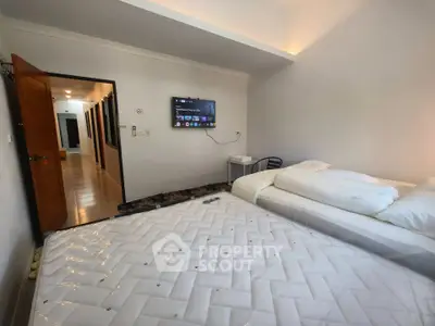 Spacious bedroom with modern TV setup and cozy bedding in a well-lit apartment.