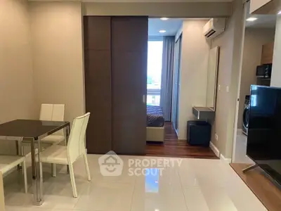 Modern apartment interior with dining area and view into bedroom, featuring sleek furniture and neutral tones.