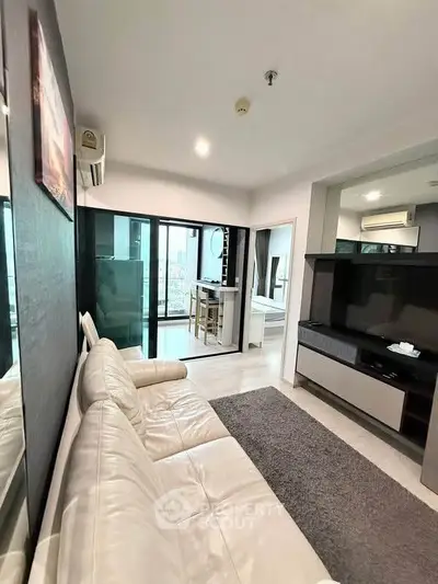 Modern living room with white leather sofa and large TV, open to a bright balcony view.