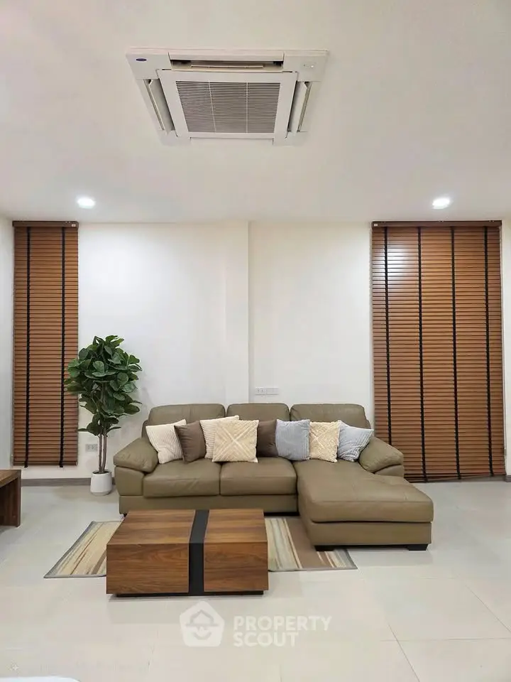Modern living room with stylish sofa, wooden blinds, and ceiling air conditioning unit.