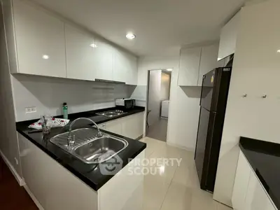Modern kitchen with sleek white cabinets and black countertops, featuring stainless steel sink and appliances.