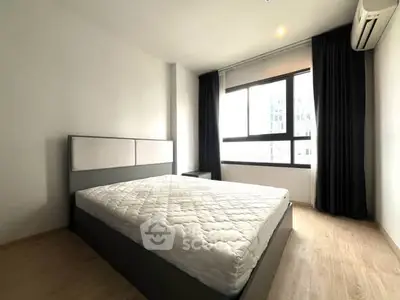 Spacious bedroom with large window and modern furnishings in a bright apartment.