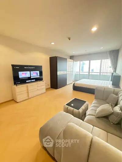 Spacious modern living room with large TV and cozy sofa, featuring a big window with city view.
