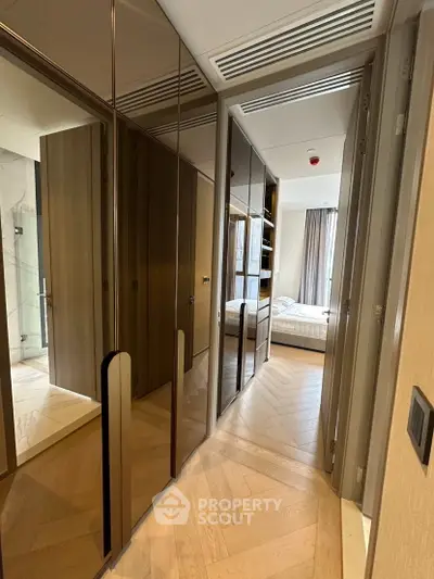 Modern apartment hallway with elegant wooden flooring and built-in storage leading to a cozy bedroom.
