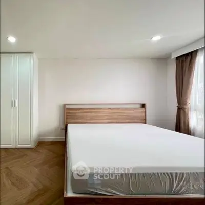 Spacious bedroom with modern wooden bed and ample natural light.