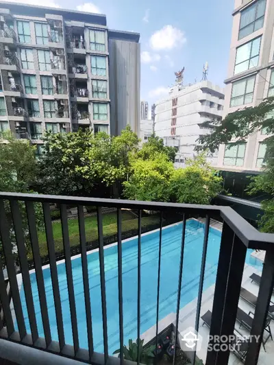 Modern apartment balcony overlooking a pristine swimming pool and lush greenery.