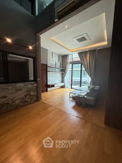 Spacious modern living room with wooden flooring and large windows offering natural light.