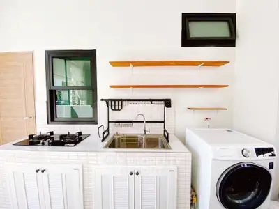 Modern kitchen with gas stove, sink, and washing machine in a sleek white design.