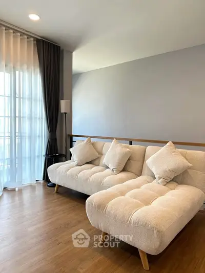 Modern living room with stylish beige sofas and wooden flooring, featuring natural light from large windows.