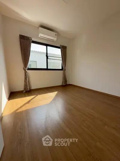 Spacious empty room with wooden flooring and large window, perfect for customization.