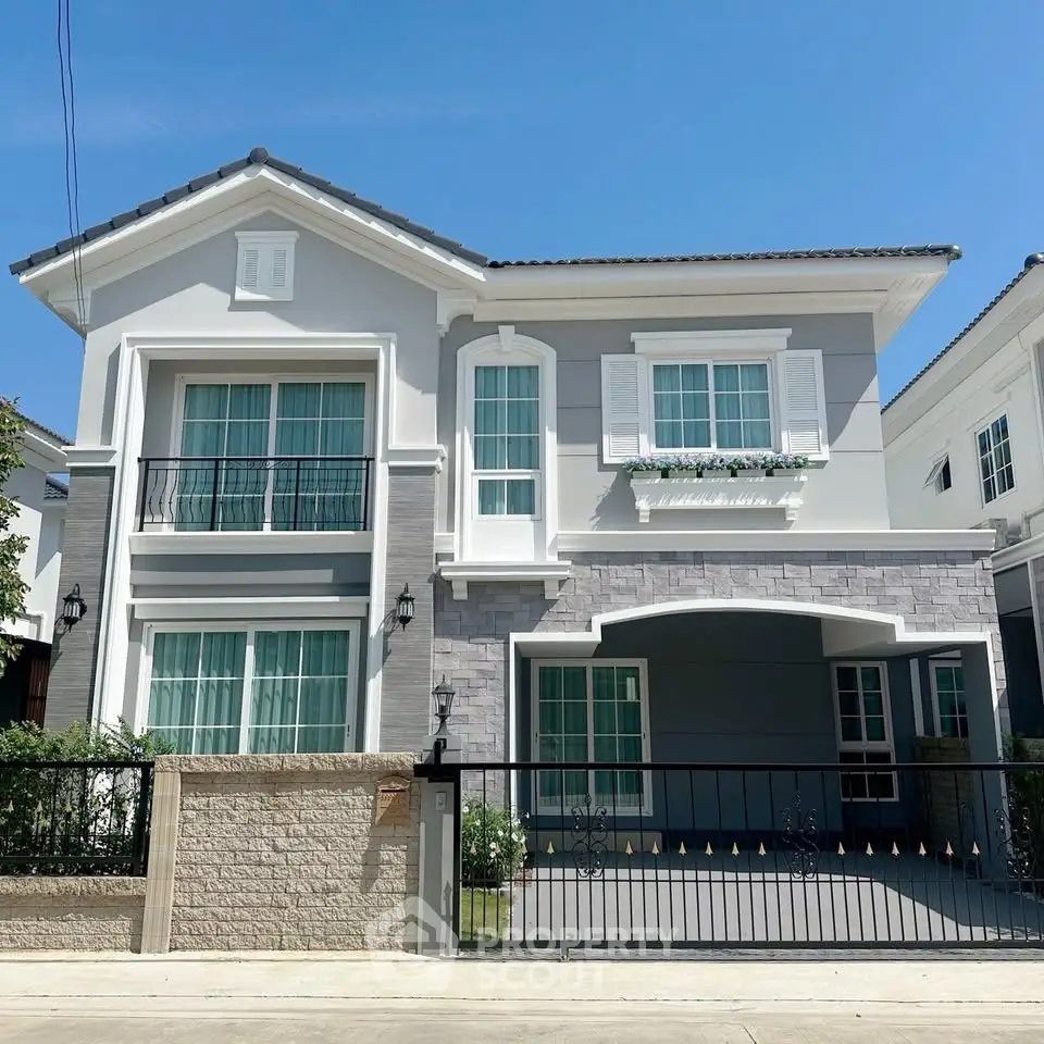 Elegant two-story house with modern facade and gated entrance under clear blue sky.